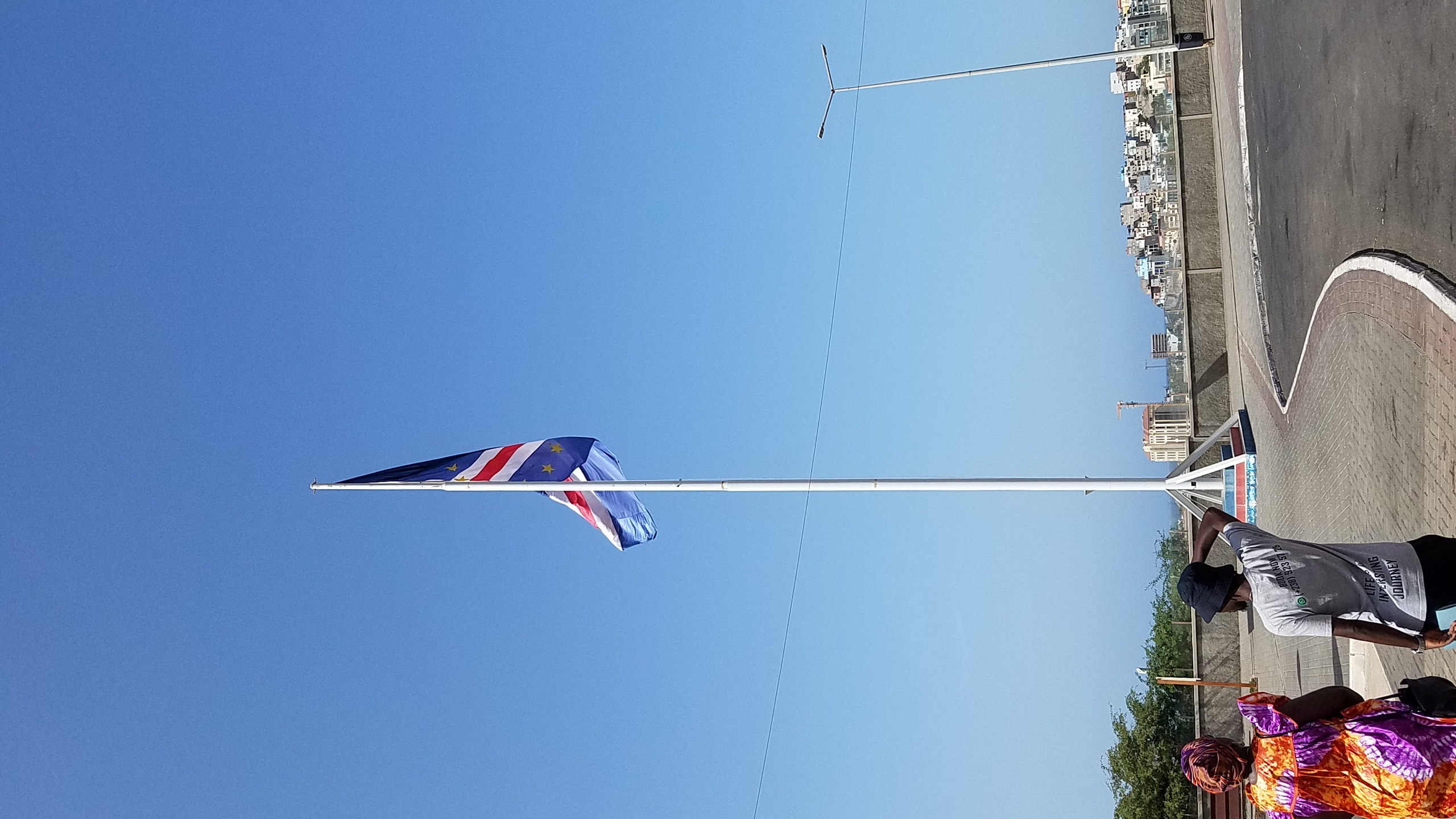 The Cabo Verde flag flying from a tall flagpole above the capital city of Praia